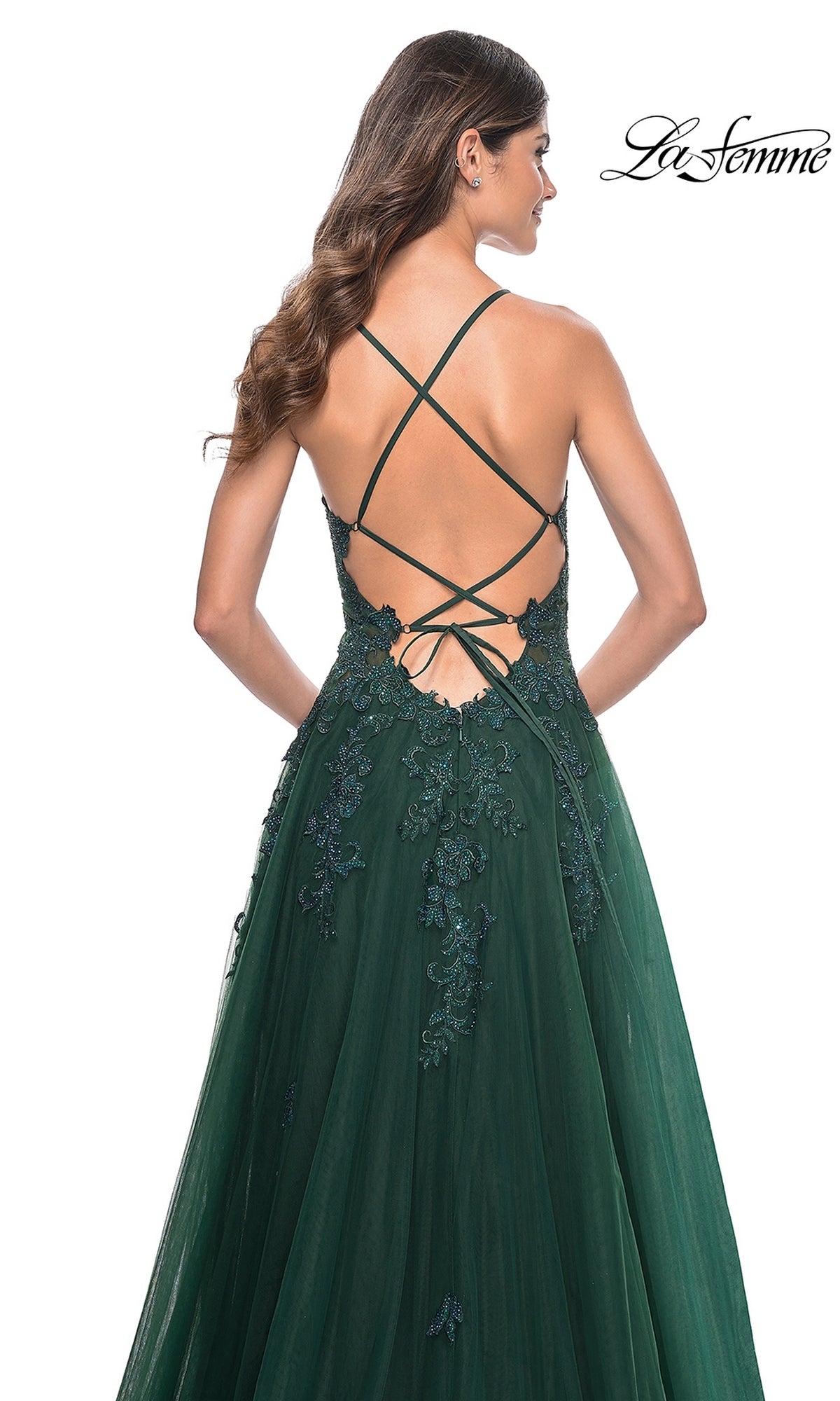 A woman wearing the La Femme Embroidered-Lace Long Prom Gown 32022 in dark green, featuring a floor-length silhouette, lace embellishments, and a crisscross open back.